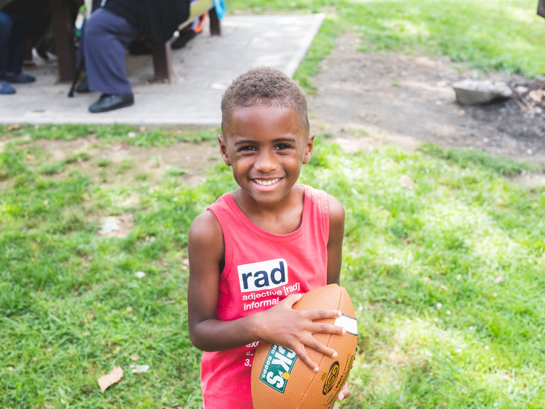 boy wears red tank top holding football ball